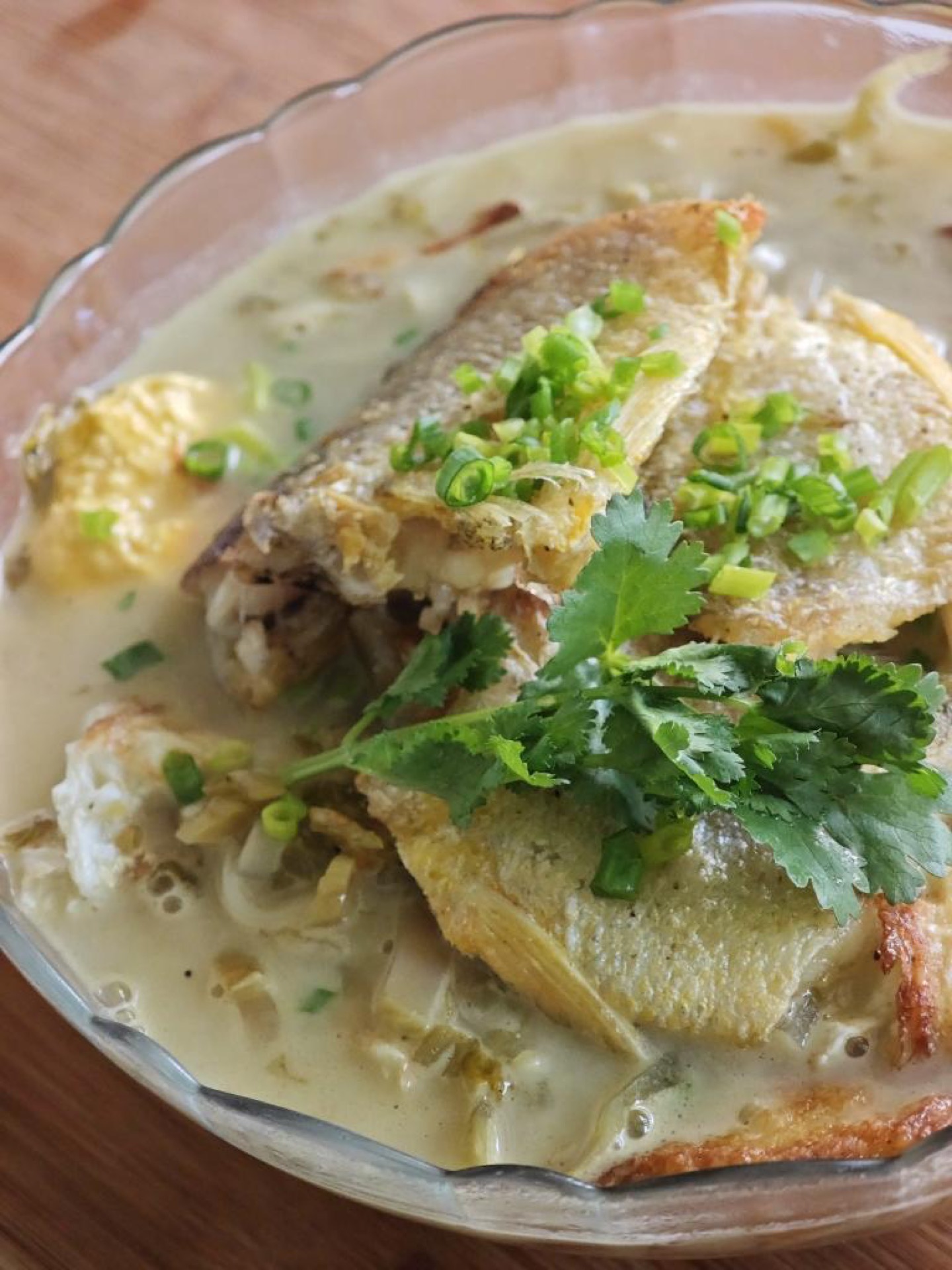 The moment it reaches the table, the milky broth is steaming, the golden fish rests on the noodles, and the green cilantro dots the surface.