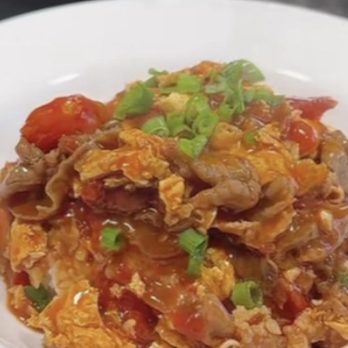 Tomato beef and egg rice bowl in a white bowl with glossy tomato sauce, tender beef slices, fried eggs and scallions over steamed rice