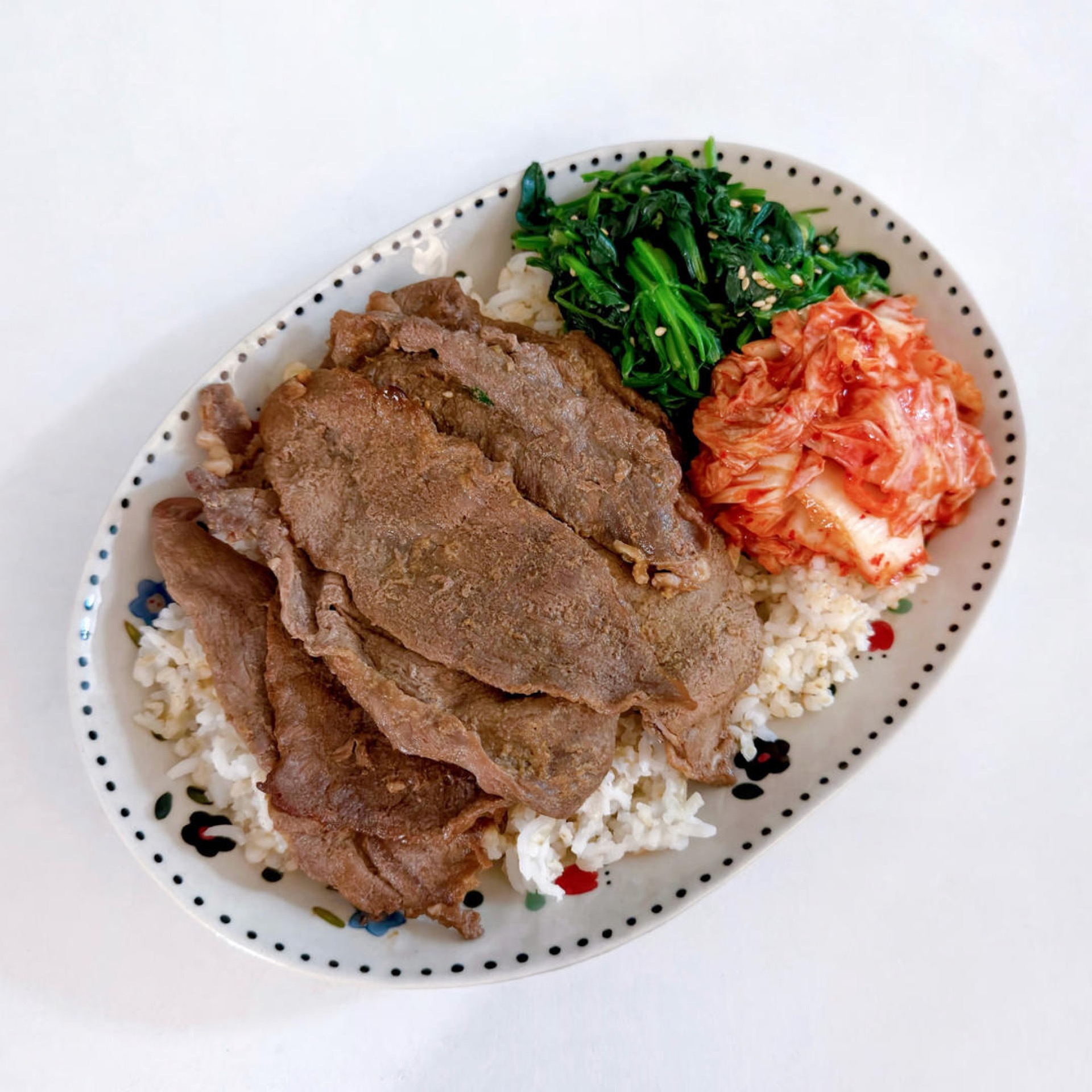 Yakiniku-style beef bento with grilled beef, sesame spinach, and kimchi over rice in a bento box